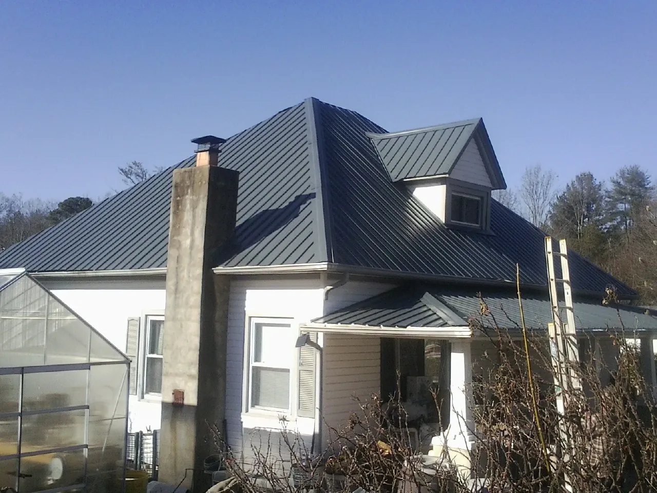 Dark blue standing seam metal roof on a white farmhouse with dormer — Slate & Tile Roof Repair by Roofing Brothers in Ryderwood