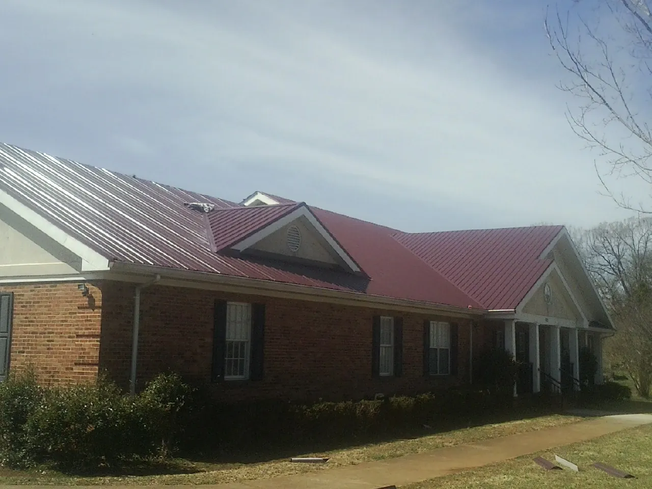 Red metal roof with gabled entries on a long brick building, from a Hail Damage Roof Repair job in Ryderwood