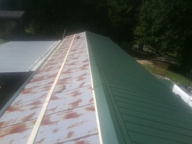 Old rusted panels beside newly installed green metal roofing — Wind Damage Roof Repair by Roofing Brothers in Ryderwood