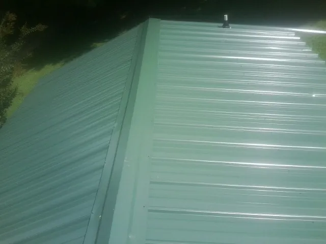 New green metal panels meeting at the ridge of a roof — Flat Roof Repair work by our crew in Ryderwood