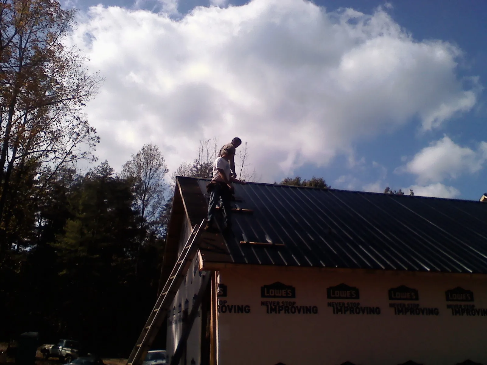 Roofer fastening dark metal panels high against a cloudy sky, from a Roof Inspection job in Ryderwood