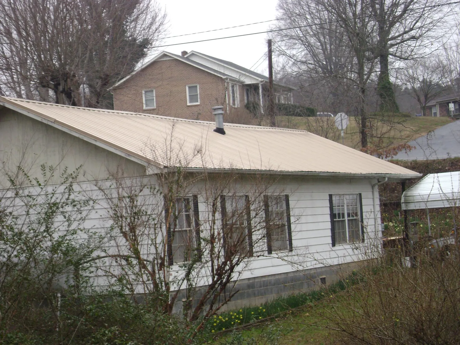 Tan metal roof on a white sided house set into a hillside — Commercial Roofing by Roofing Brothers in Ryderwood